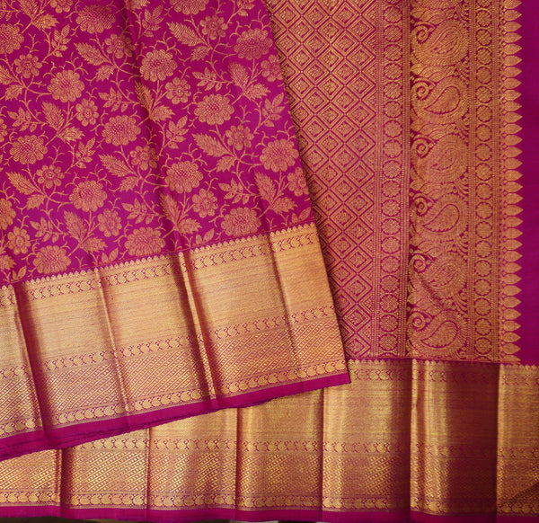 A close-up of a rich magenta pink and gold Banarasi silk saree, showcasing its floral zari embroidery, detailed border patterns, and metallic gold weave.
