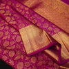 A close-up of a rich magenta pink silk fabric with intricate gold zari floral patterns and a wide gold border.