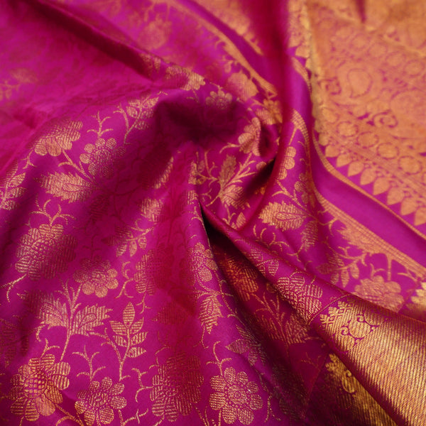 A close-up of a rich magenta pink fabric with intricate gold floral brocade patterns and a matching gold border.