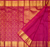 A close-up of a rich magenta pink and gold woven fabric, likely a silk saree, showing a detailed floral pattern on the body, a smooth magenta section, and a wide gold zari border.