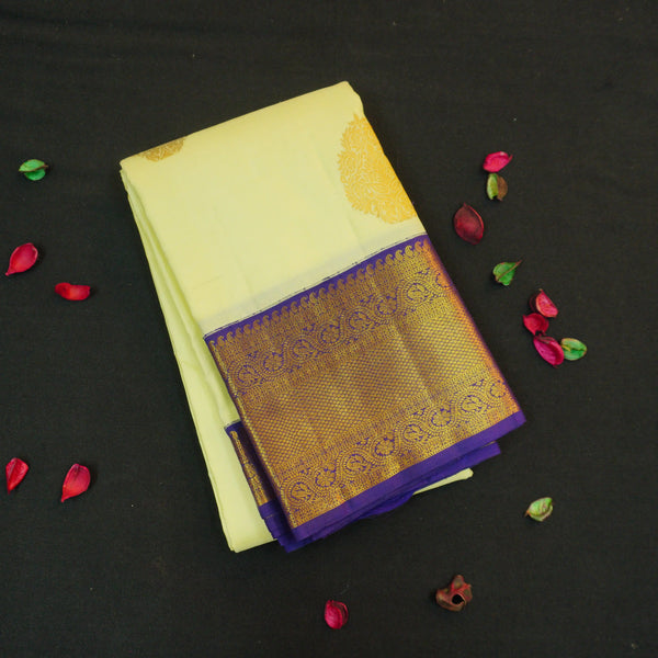 Lemon yellow vintage Kanchipuram silk saree with navy blue korvai border, featuring gold floral thilagam motifs on the body and a richly woven traditional zari pallu.