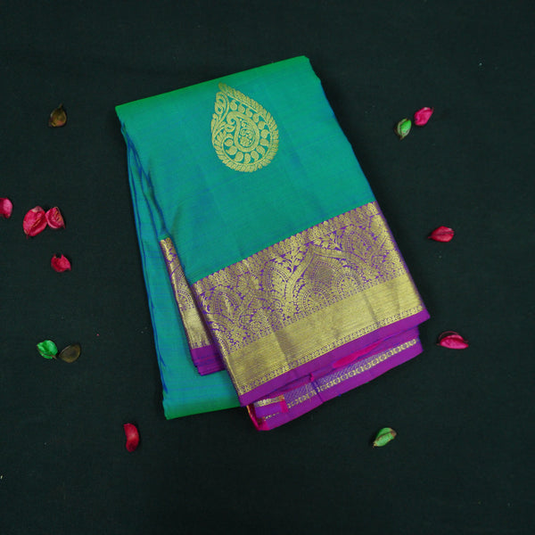 Peacock blue Kanchipuram silk saree with gold zari thilagam butta motifs, violet border, and rich woven pallu – traditional bridal silk saree by Vivaaha Silks.