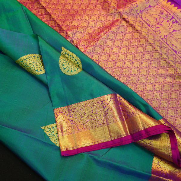 Peacock blue Kanchipuram silk saree with gold zari thilagam butta motifs, violet border, and rich woven pallu – traditional bridal silk saree by Vivaaha Silks.