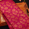 A close-up of a rich magenta pink brocade fabric with an intricate gold floral pattern, draped over a carved wooden tray.