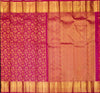 A close-up of a richly patterned silk saree, likely a Banarasi, featuring a magenta-pink body with intricate gold zari floral motifs on one side, a peach-pink body with delicate gold woven borders on the other, and a wide gold zari border at the top and bottom.