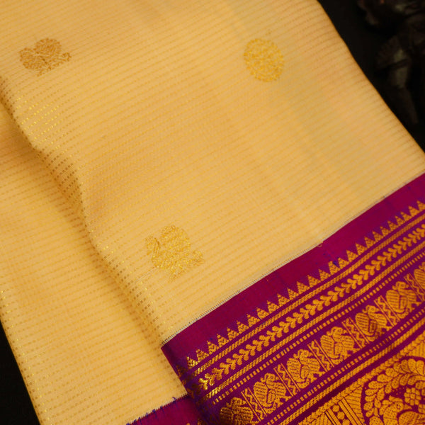 A close-up of a Cream silk saree body with subtle woven motifs, featuring a rich magenta and gold zari border.
