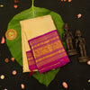 A folded cream-colored silk saree with a vibrant magenta and gold zari border, displayed on a large green leaf over a black background with decorative elements.