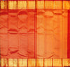 A close-up of a richly colored fabric, likely a sari, featuring a dominant redbody with a golden-yellow border and subtle woven patterns.