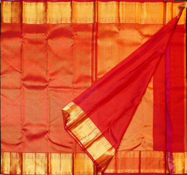 A close-up of a red silk saree with a wide gold zari border, folded diagonally to show the fabric texture and pallu.