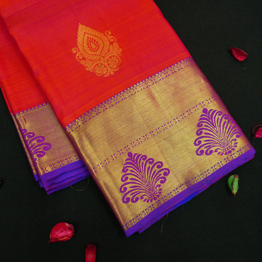 Tomato red Kanchipuram silk saree with violet zari border and pallu, featuring gold thilagam motifs.